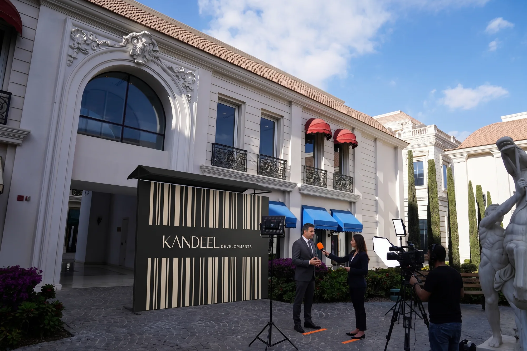 TV interview at the Kandeel Developments media wall by the arched entrance, camera, LED lights and mic flag